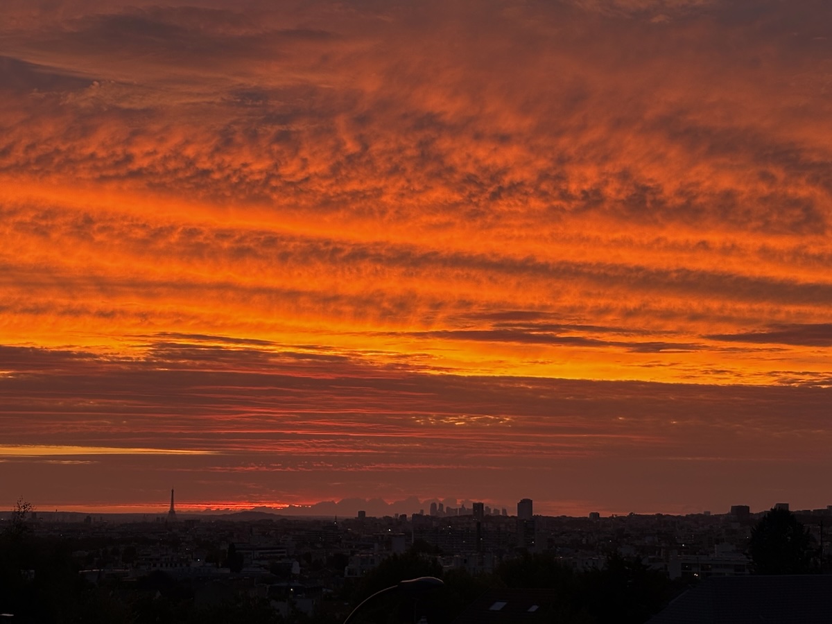 Ciel flamboyant au-dessus de Paris avec la silhouette de la tour Eiffel et du quartier de La Défense à l’horizon