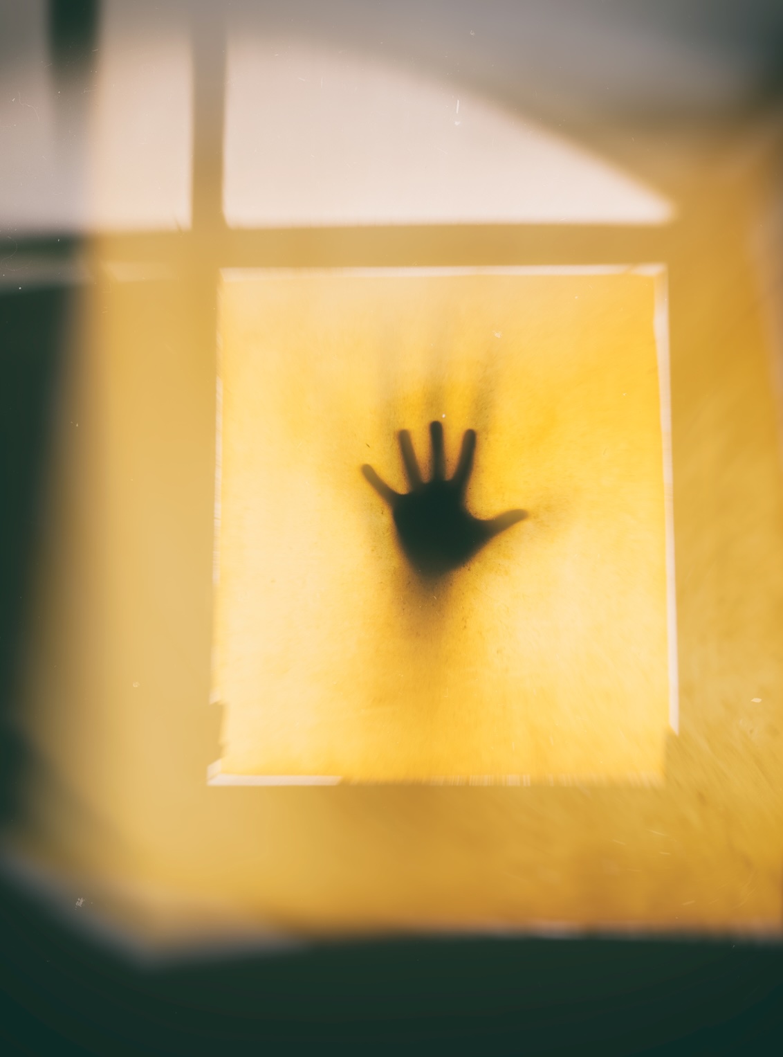 Silhouette d’une main posée contre une vitre translucide baignée de lumière jaune symbolisant le blocage
