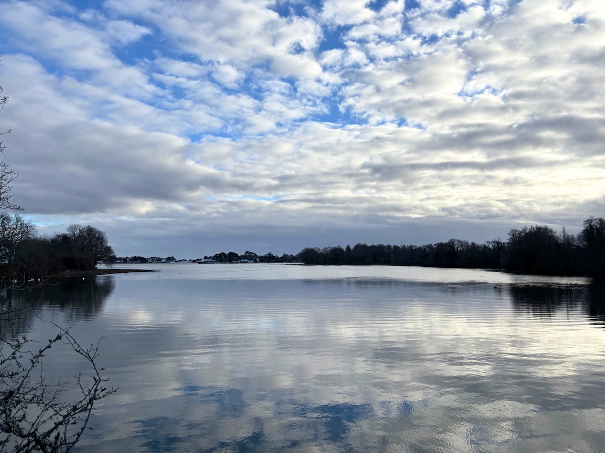 Anse de Penfoulic à marée haute, eau calme reflétant un ciel d’hiver parsemé de nuages blancs
